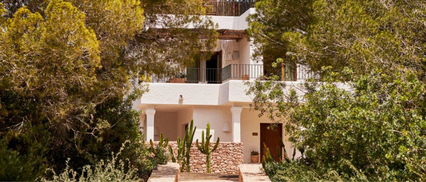 Two-storey white villa-style building shrouded in greenery with white walls and exposed stone finishes