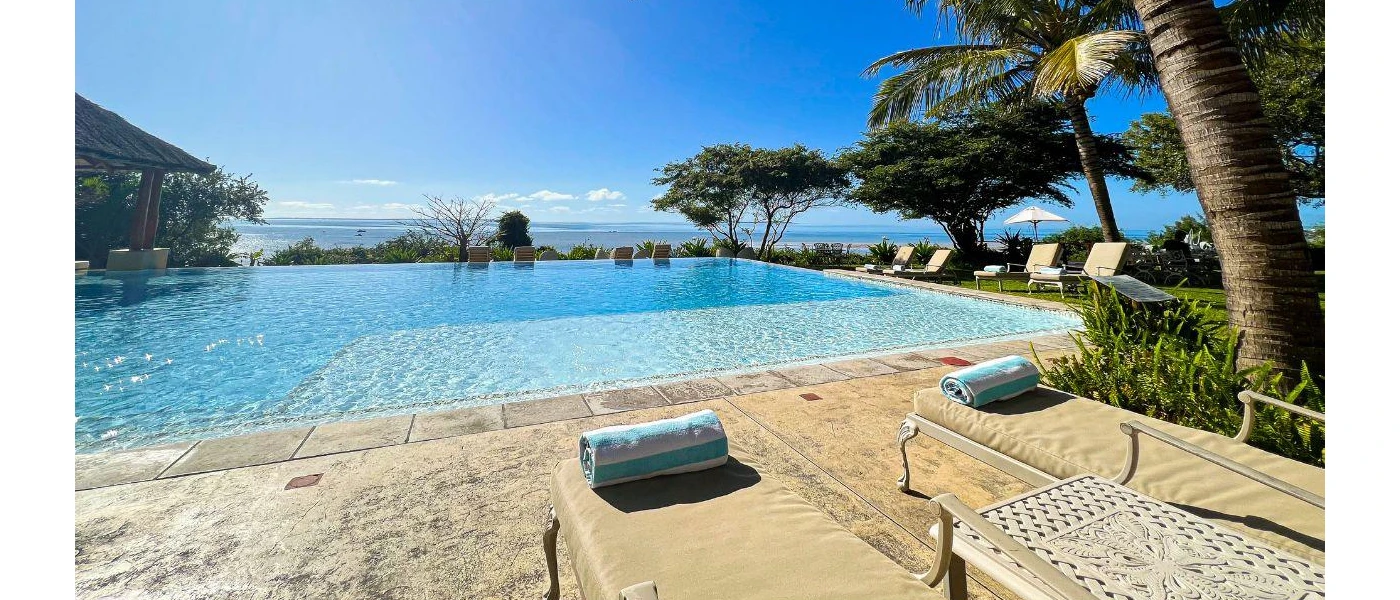 Infinity swimming pool surrounded by trees and loungers with blue towels on them