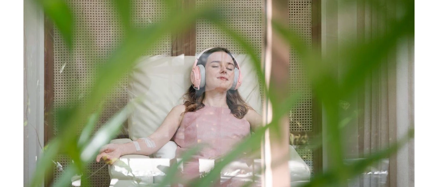 Smiling woman relaxes in headphones with her eyes closed, while sitting back and being treated with a drip