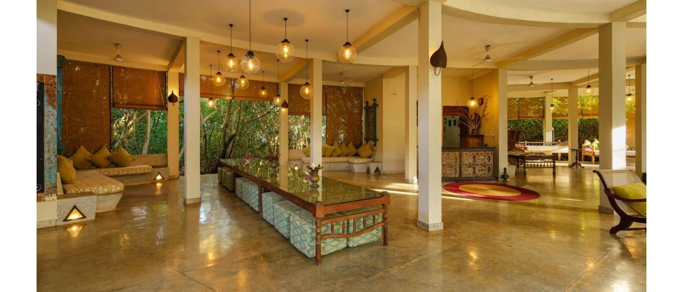 Airy, bohemian-style lobby area, with tiled floors, hanging lightbulb-style ceiling lights, rattan-style blinds and patterned cushions