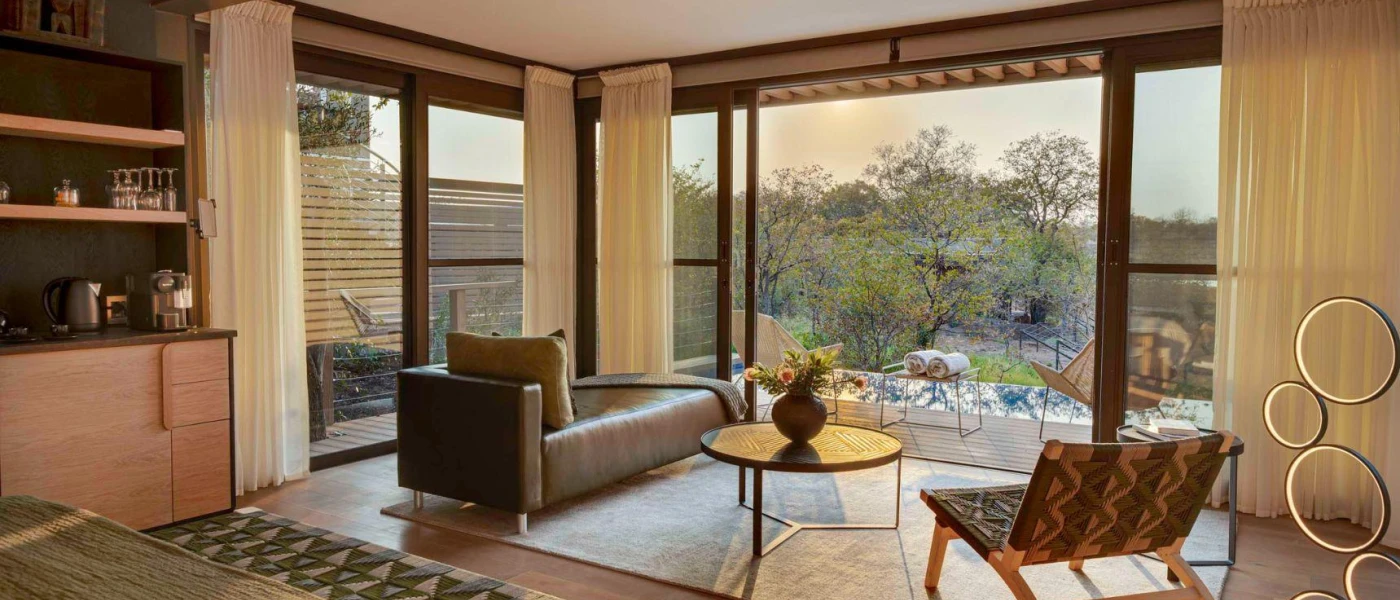 Lodge living area with a chaise longue-style sofa, rug and chair in aztec-style prints overlooking a furnished balcony with pool and reserve views