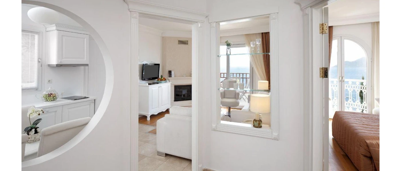 Bright hotel room with white walls and ceilings, furniture and a TV, with separate living room and bedroom