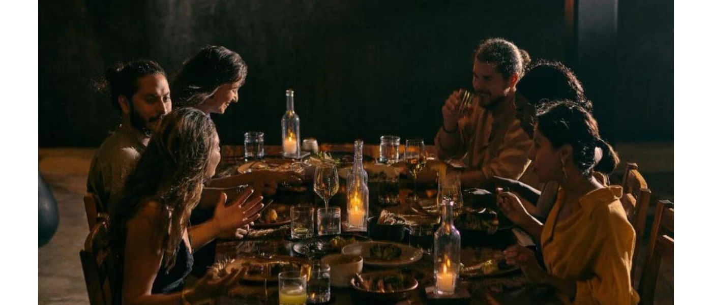 Group sit around a candlelit wooden table enjoying a meal at night-time