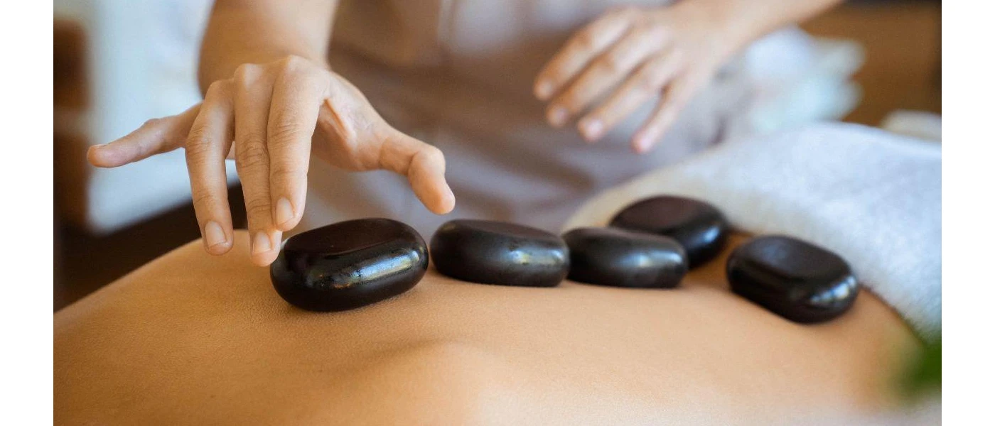 Therapist places black stones on the back of a guest lying on their front in a towel