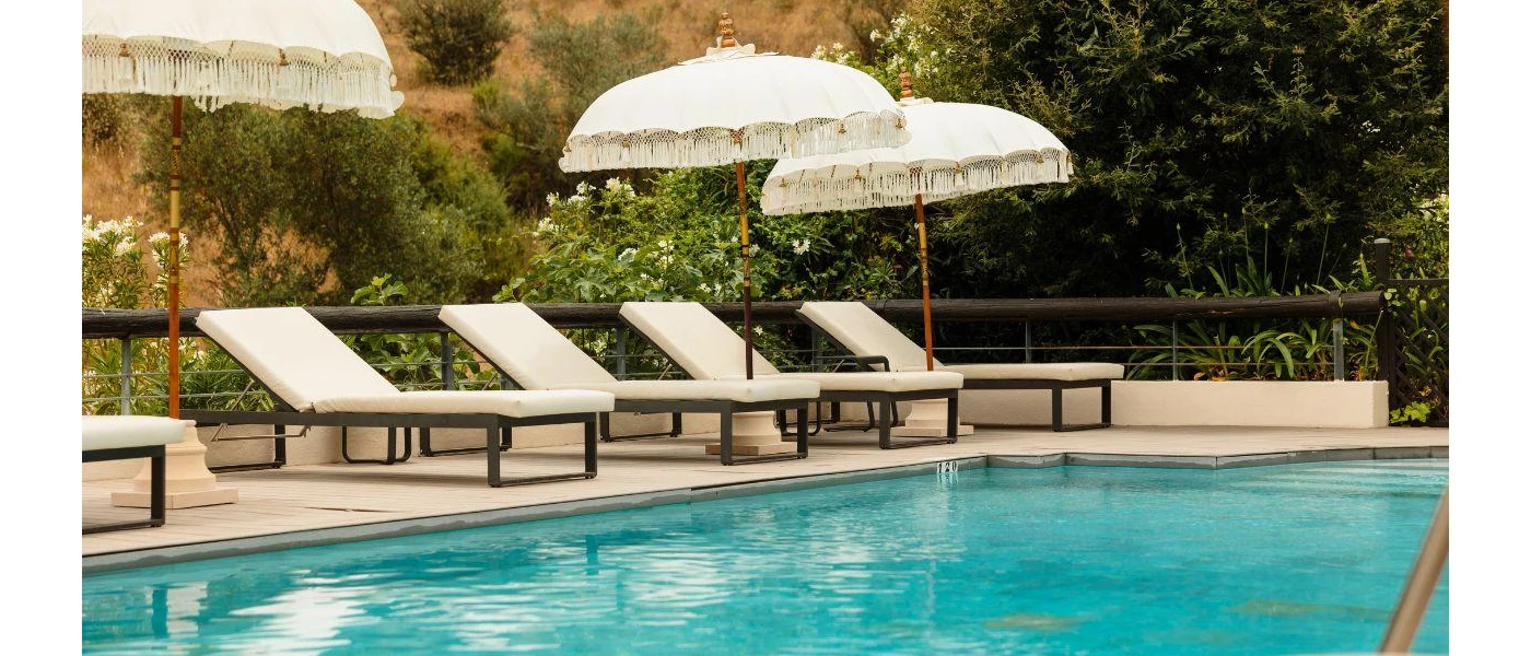 Swimming pool lined with white-cushioned loungers and boho-style white umbrellas with fringing