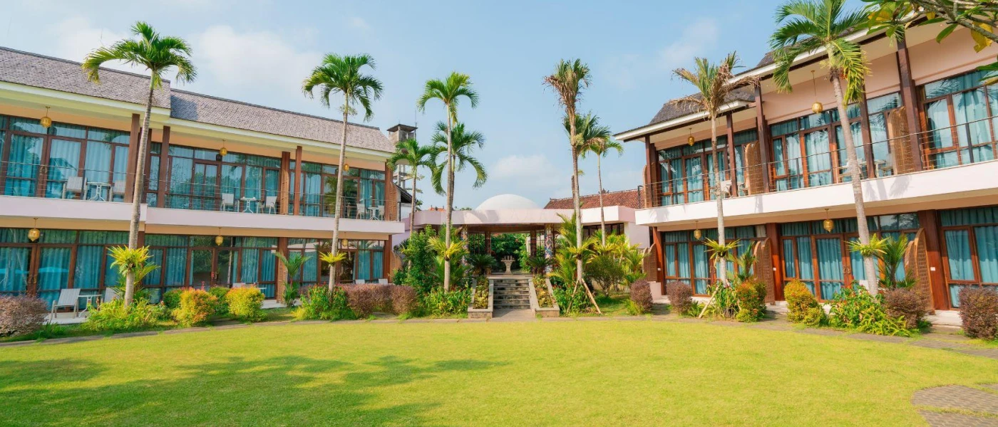 Two-storey peach buildings overlooking a grassy lawn lined with palm trees