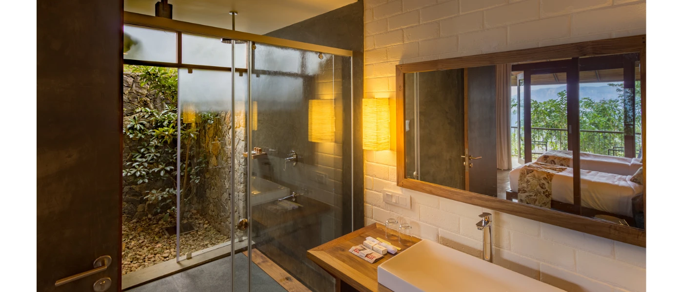 Glass-walled shower showing gardens outside, a vanity unit with a large white sink and a mirror on the wall