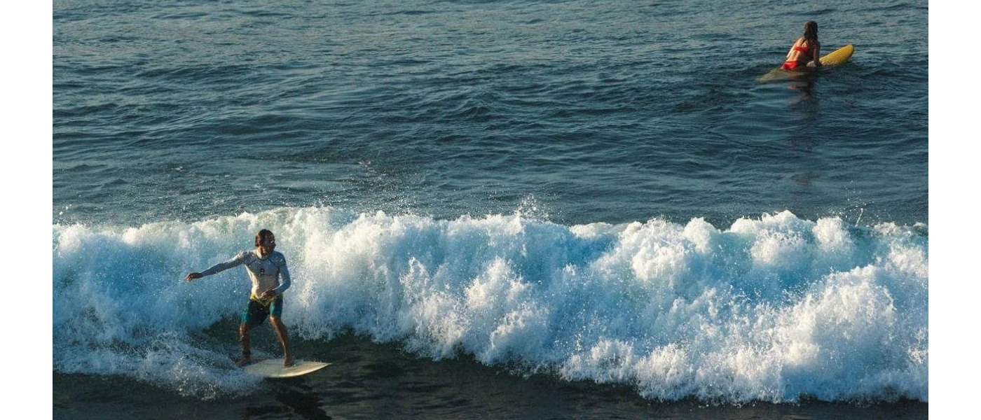 Man and woman on surf boards, one standing one paddling, in the ocean