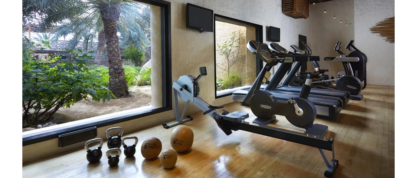 Treadmills, a bike, a rower and weights in front of floor-to-ceiling windows and tropical greenery beyond
