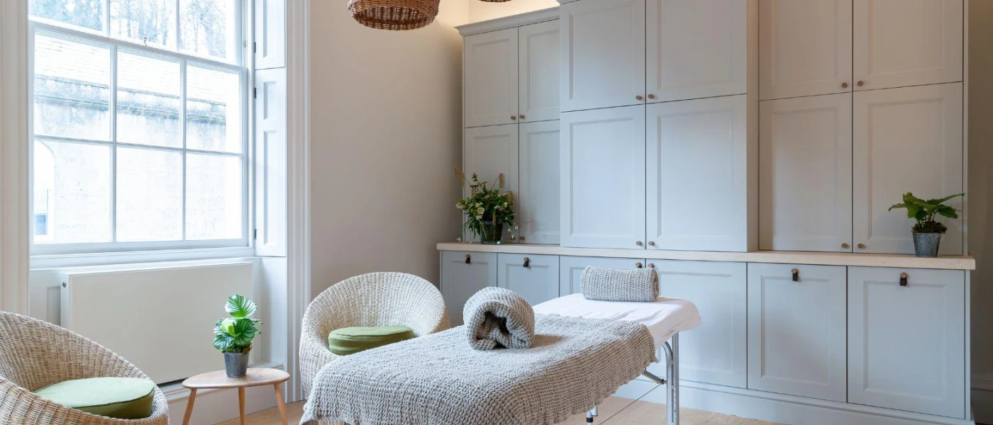 White treatment room with a bed, cupboards and a chair