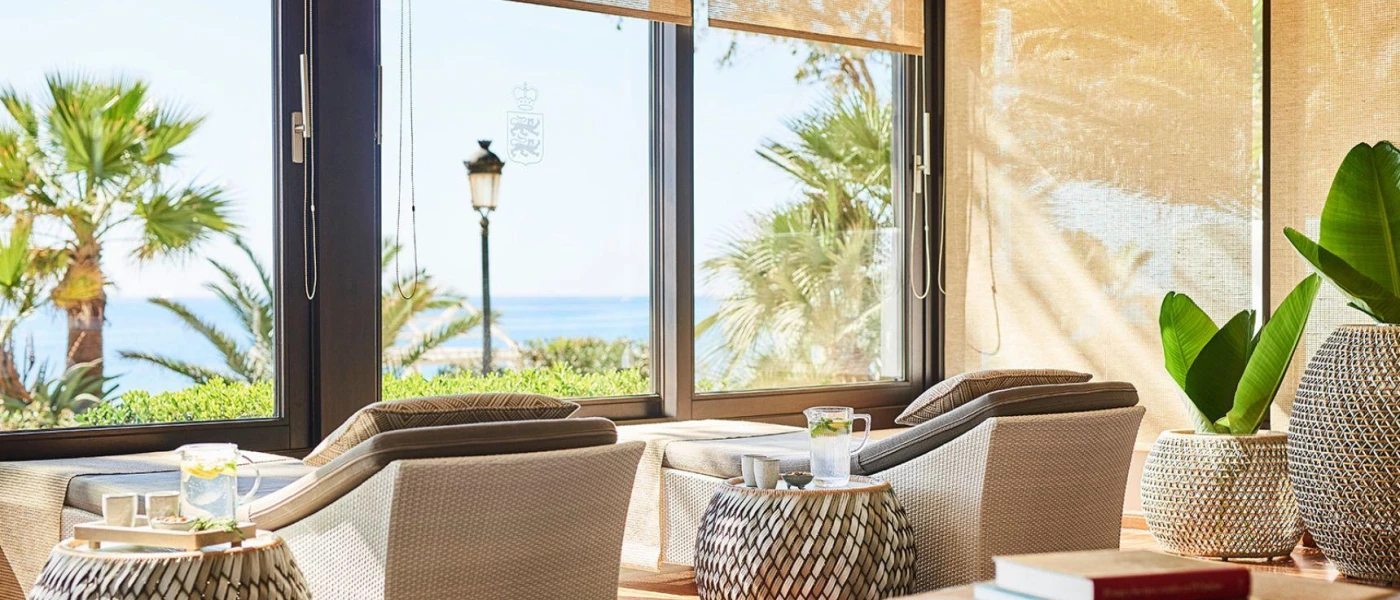 Rattan loungers next to stalls with jugs of fruit water, in front of large windows overlooking the sea