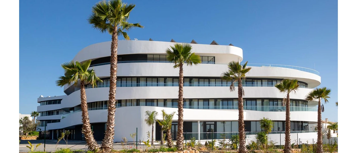 Tiered, rounded white multi-storey exterior of Longevity Health & Wellness Hotel, designed to look like a wave under a blue sky