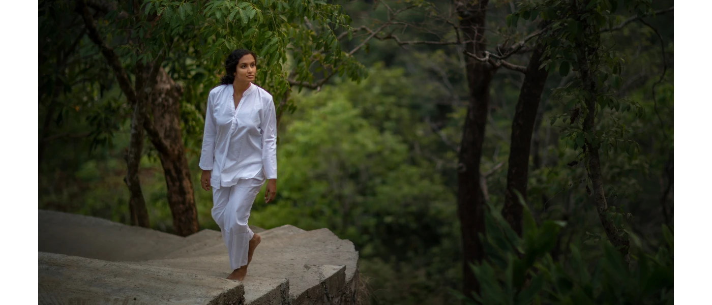 Woman in white strolls up a stone staircase surrounded by forest greenery