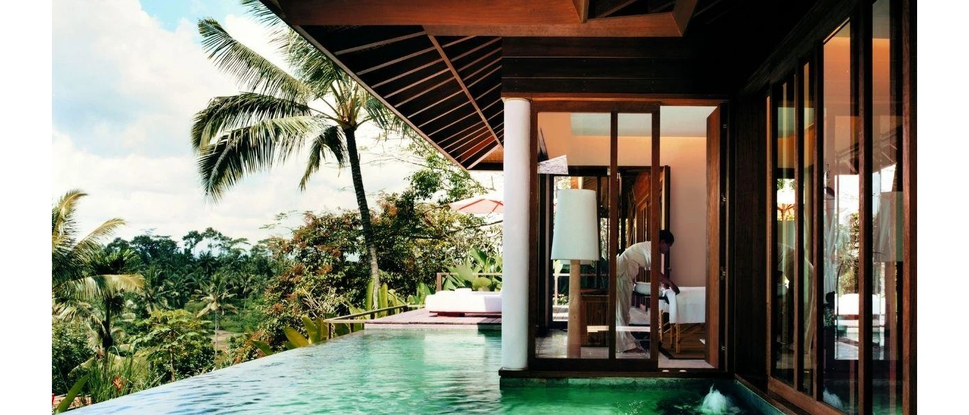 Staff member making the bed in a hotel room with its own infinity pool and furnished terrace just in front