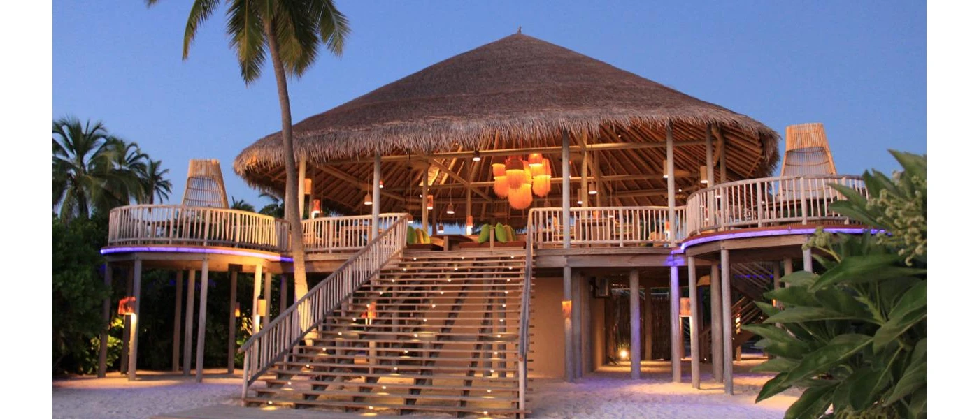 Wooden steps leading up to a thatched-roof building with a wraparound balcony, and hanging lantern-style pendant lights