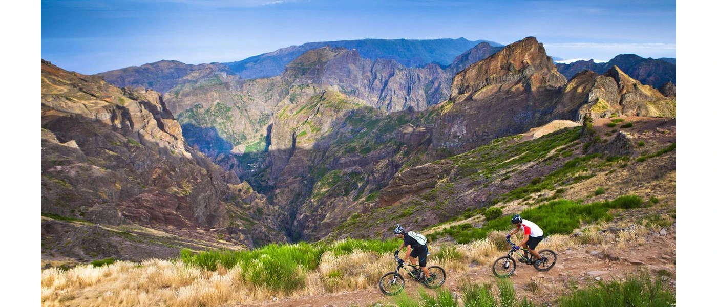 Two people in active wear cycle in the mountains under a blue sky