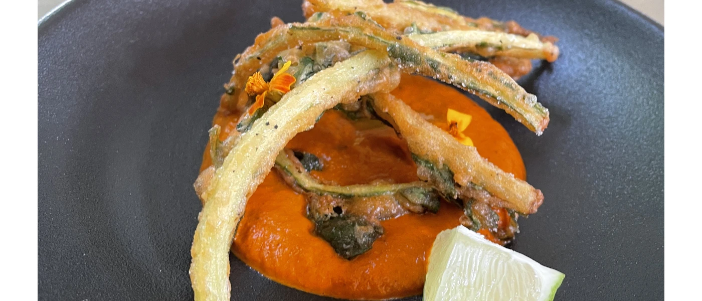 Battered vegetables on an orange puree-like sauce with edible flowers on a dark grey plate