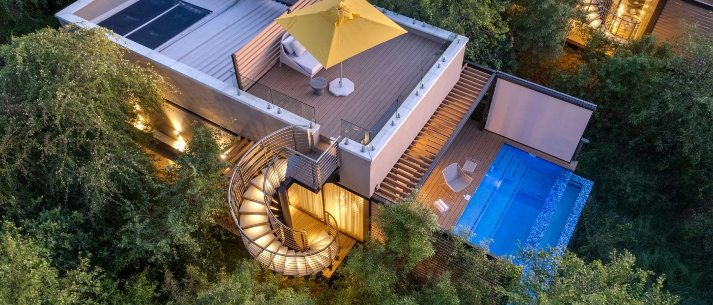 Lodge with wooden decking, a spiral staircase leading to a rooftop deck, a lower-level swimming pool and reserve surroundings