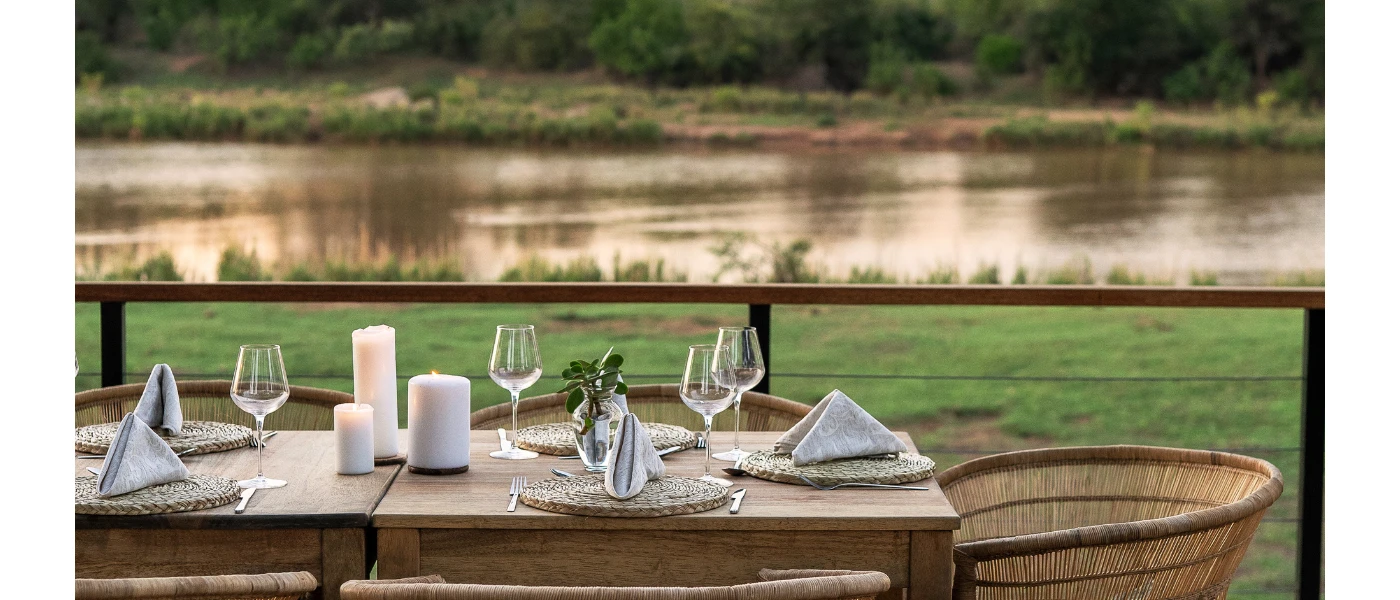 Table laid up with glassware, white napkins and candles with a view of the riverbank