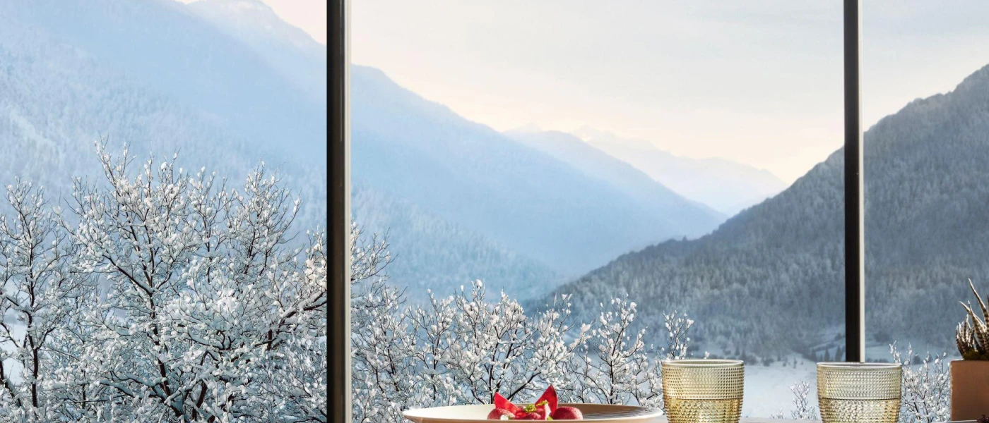 Table laid out with cups and plates in front of a window with a view of snowy woodland and mountains