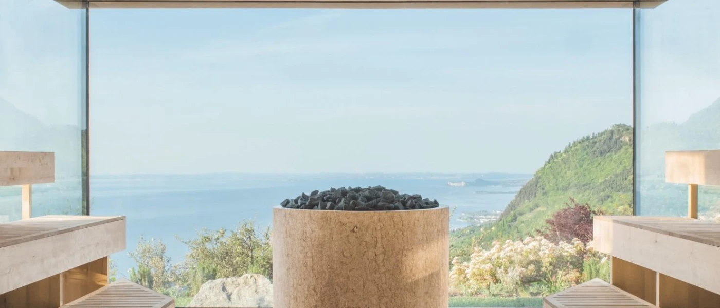 A wooden sauna with huge window overlooking a lake and green mountains