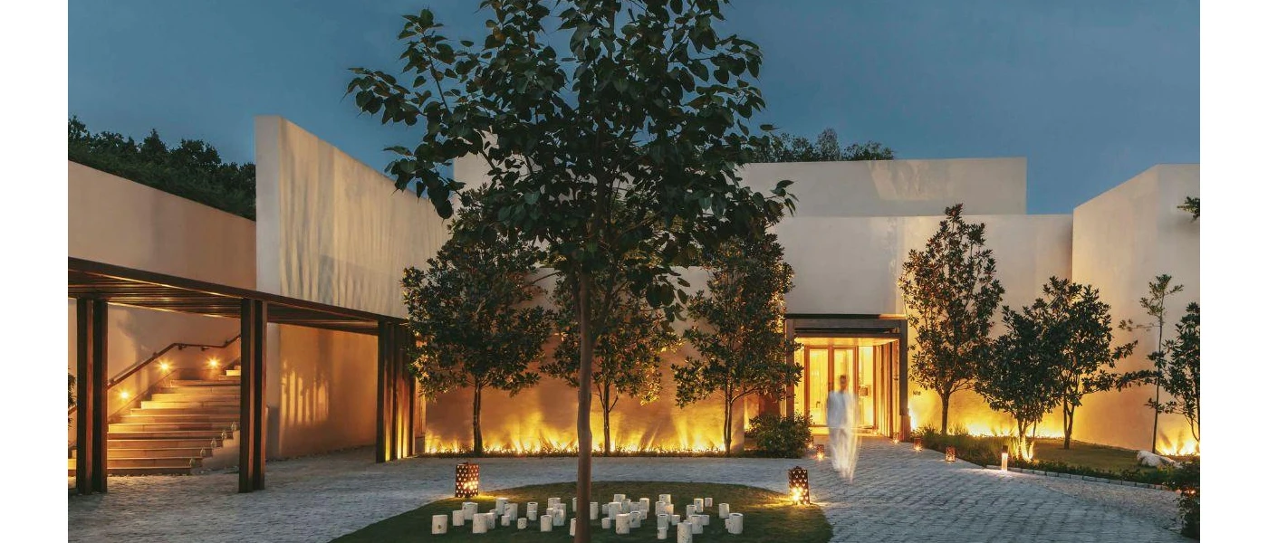 Man in white walks through a central courtyard with trees, paved concrete and lanterns as the sky gets darker