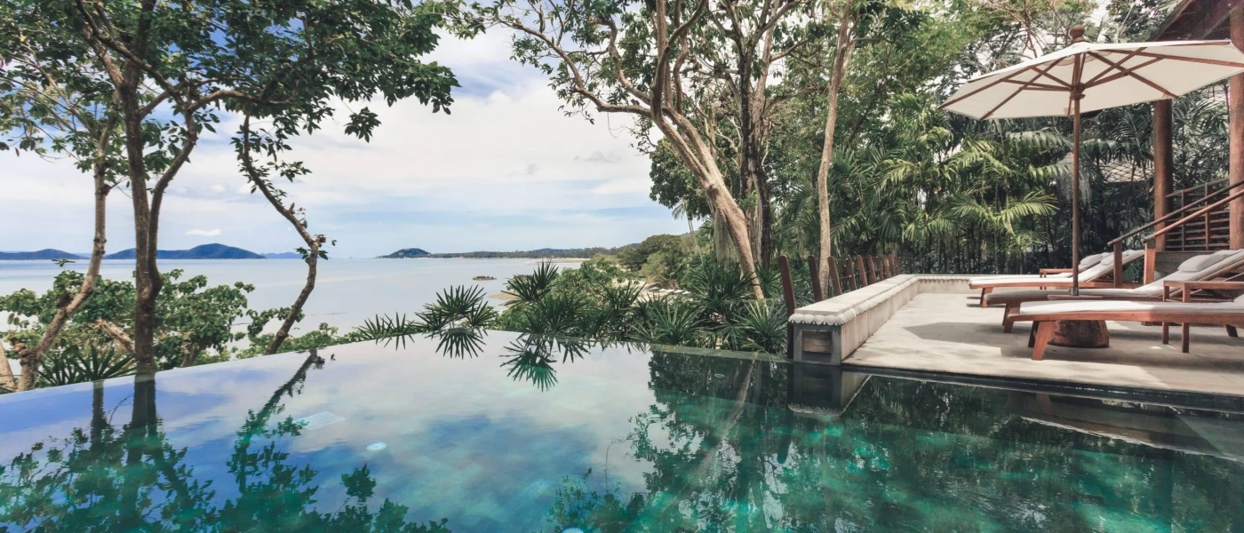 Infinity-edge pool surrounded by loungers, parasols and tropical gardens 