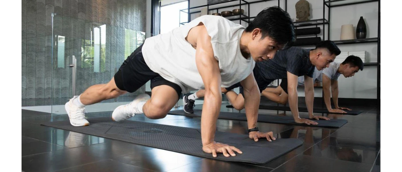 Three men in active wear in a plank position on yoga mats in an airy studio