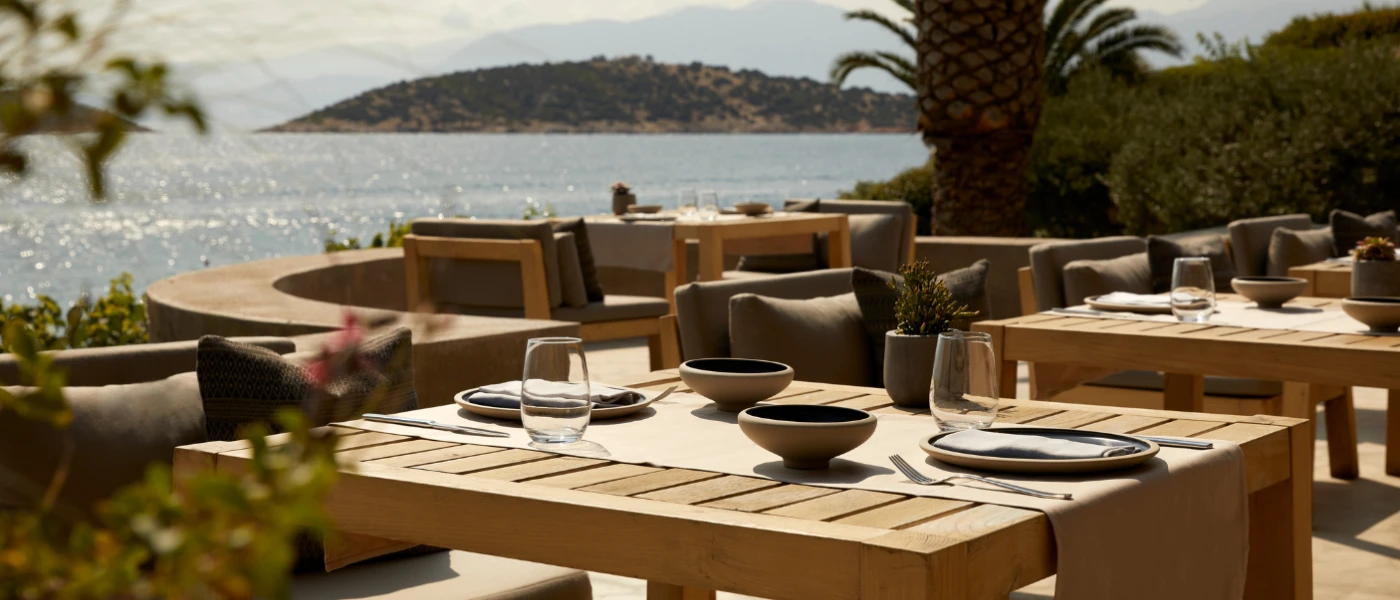Oceanfront terrace with square wooden tables and chunky armchair-style grey chairs