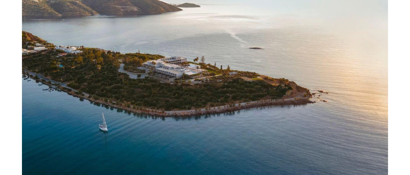 White resort on a peninsula cloaked in greenery surrounded by the sea and mountains