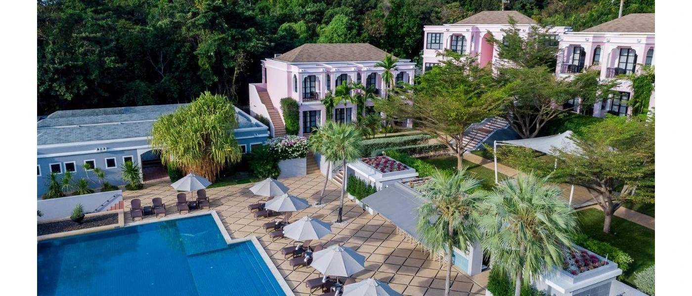 Pink multi-storey buildings surrounding a swimming pool and paved terrace, with tropical palms and greenery