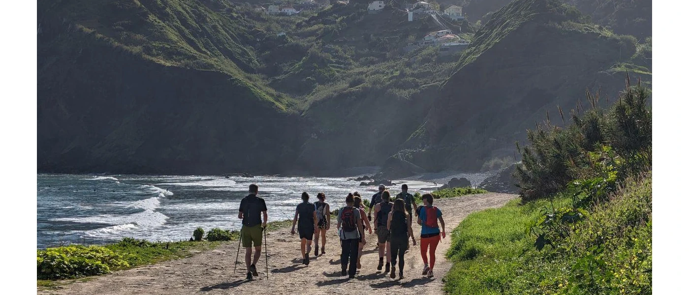 Group of people hiking next to water and surrounded by green mountains 