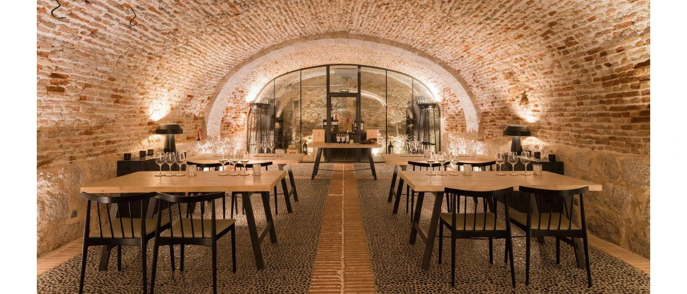 Underground wine cellar and tasting area, with stone walls, wooden tables and chairs, and empty glasses ready for guests