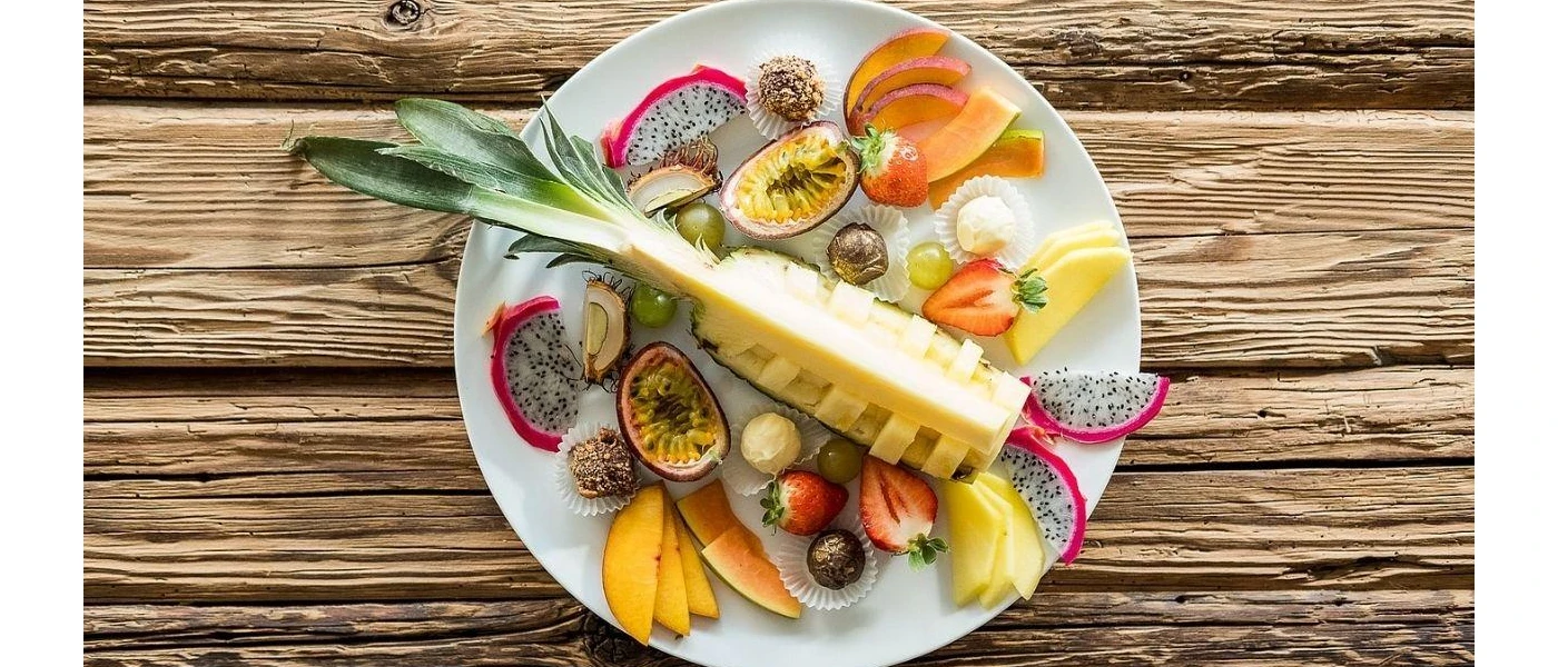 White plate piled with fruit including pineapple, peaches and strawberries