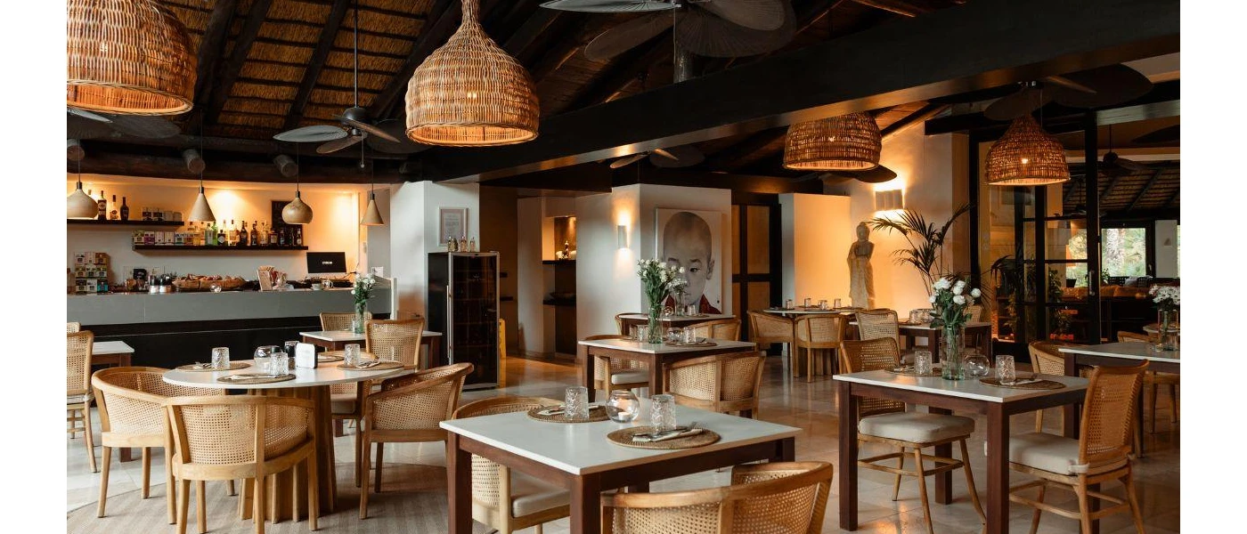 Rustic, boho-style restaurant with rattan lantern ceiling lights, wooden tables and chairs, wood-beamed ceilings and a Buddha statue 