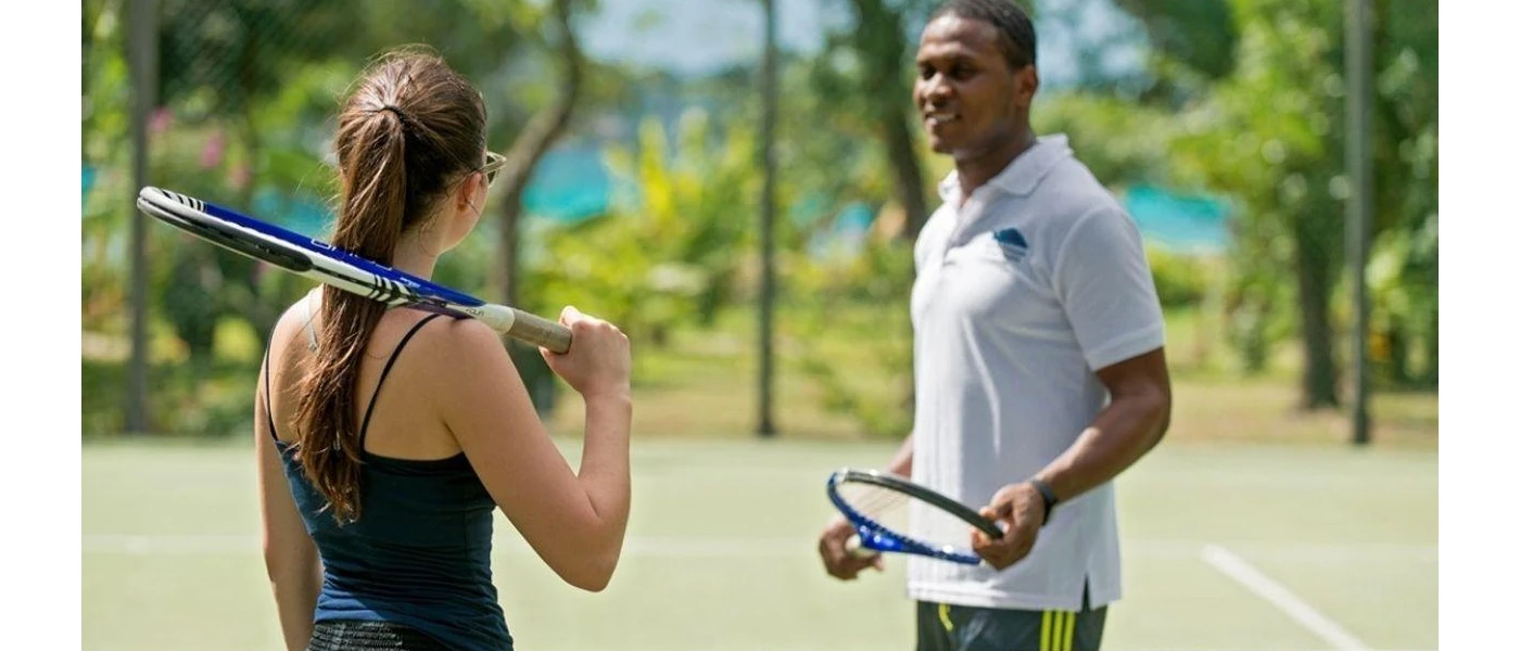 Woman with a tennis racquet standing next to a man with a tennis racquet on an ocean-facing court 