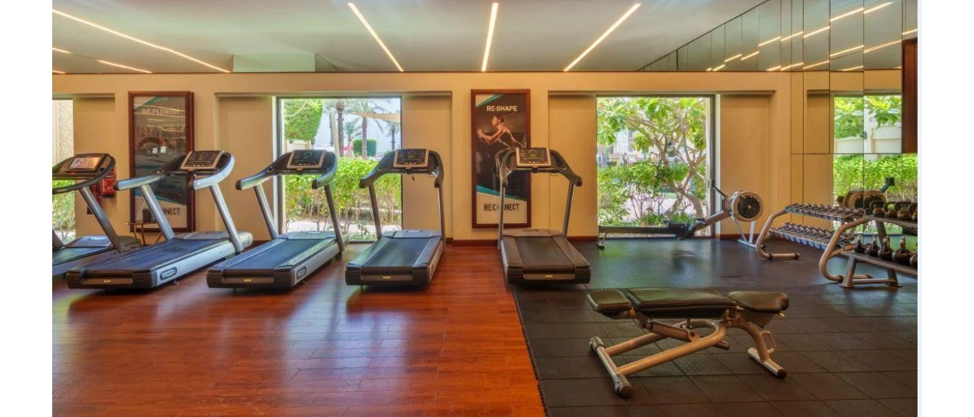 Gym with wooden and mat flooring with treadmills, benches and floor-to-ceiling windows 