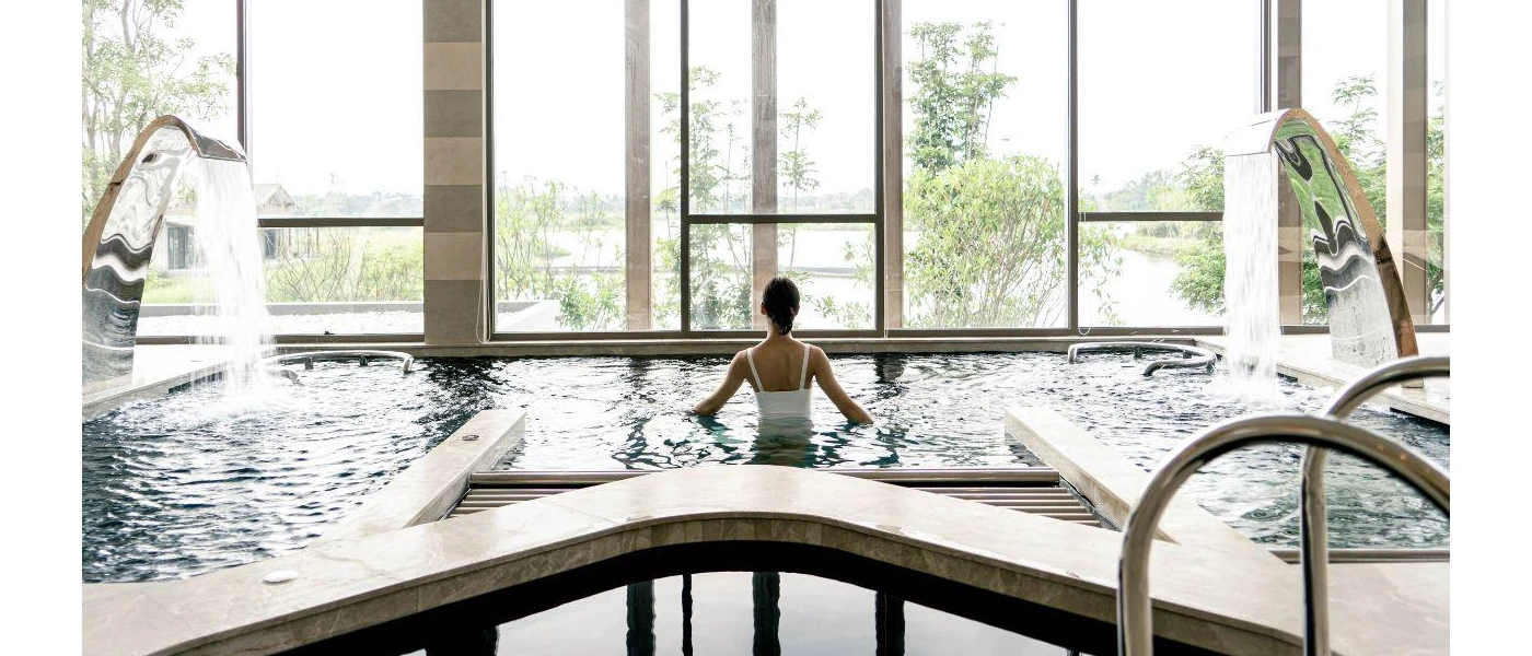 Woman in a white swimsuit relaxes in an indoor pool with floor-to-ceiling windows