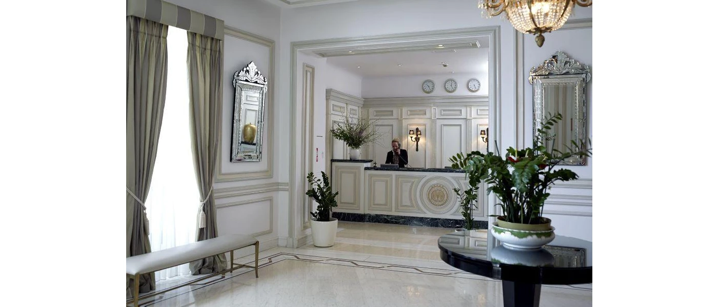 Elegant reception area with antique-style mirrors, a wooden round table with a vase of flowers, neutral rooms and potted plants