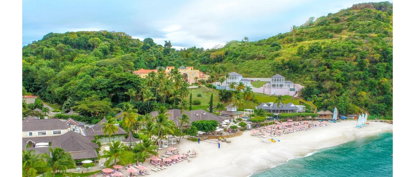 Sprawling grey-roofed resort among lush greenery overlooking a white-sand beach