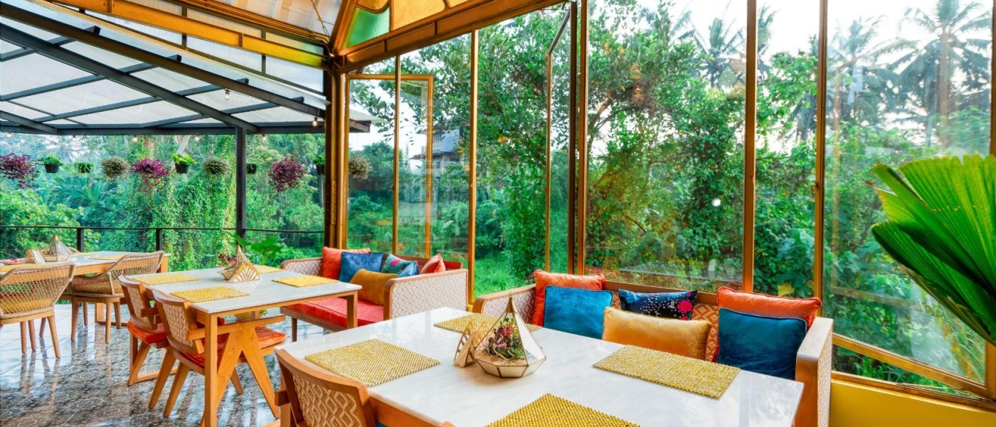 Restaurant with wooden tables and seating with colourful cushions, overlooking tropical gardens