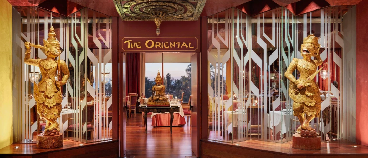 Dark-wood restaurant entrance with two matching gold statues and the words 'The Oriental' etched above the door