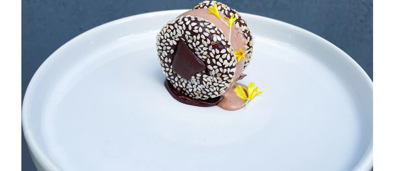 Bitesize dessert on a white plate, with a white seeded covering and edible yellow flowers