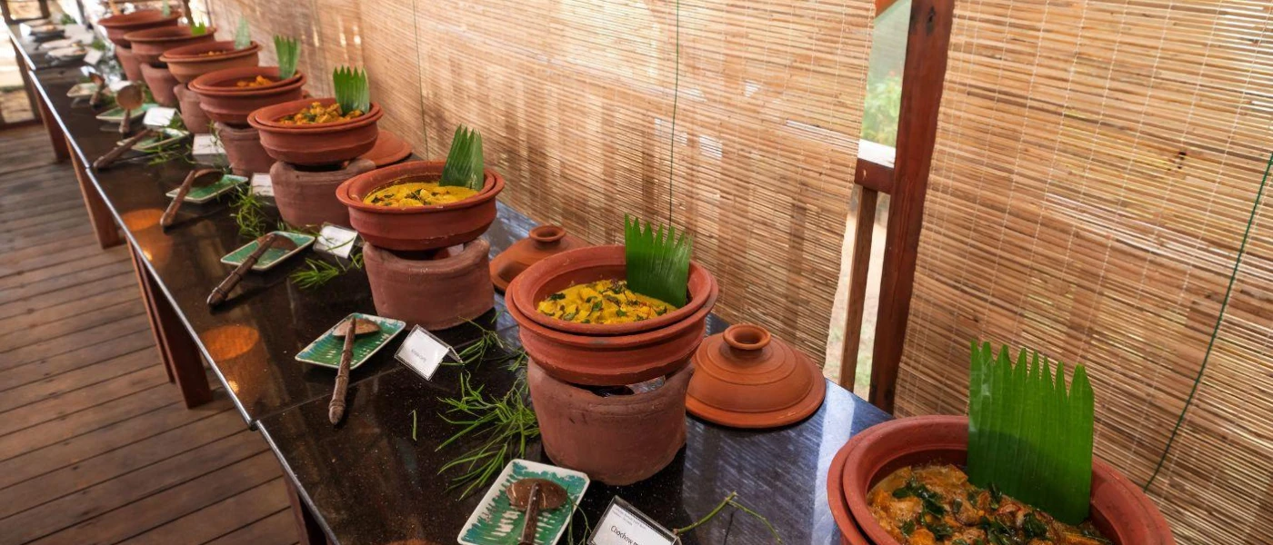 Terracotta bowls lined up on a long table, filled with curries and fronted by labels 