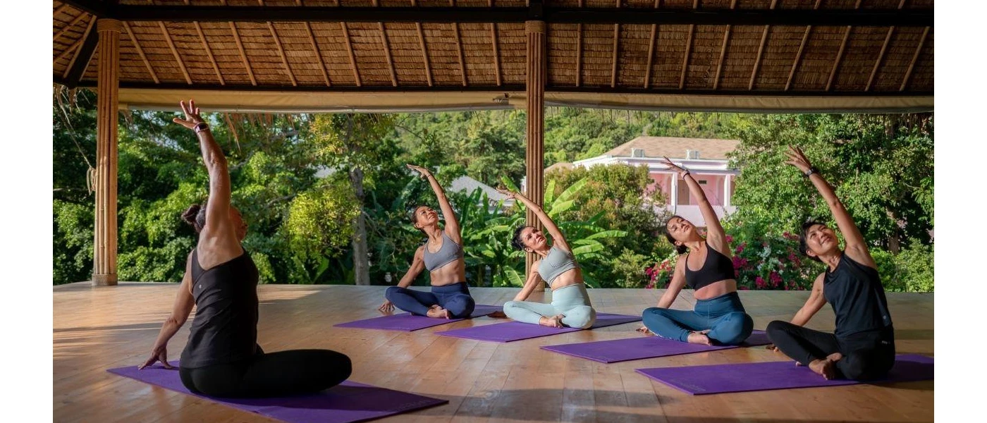 Group stretching on purple yoga mats in an open-sided thatched-roof pavilion