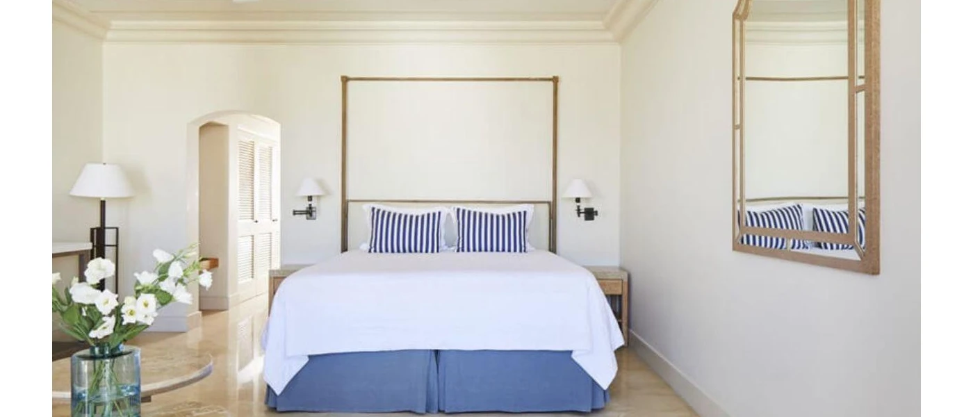 Stylish bedroom with crisp white bedding, blue and white pinstriped cushions and a wooden table with a glass vase with white flowers