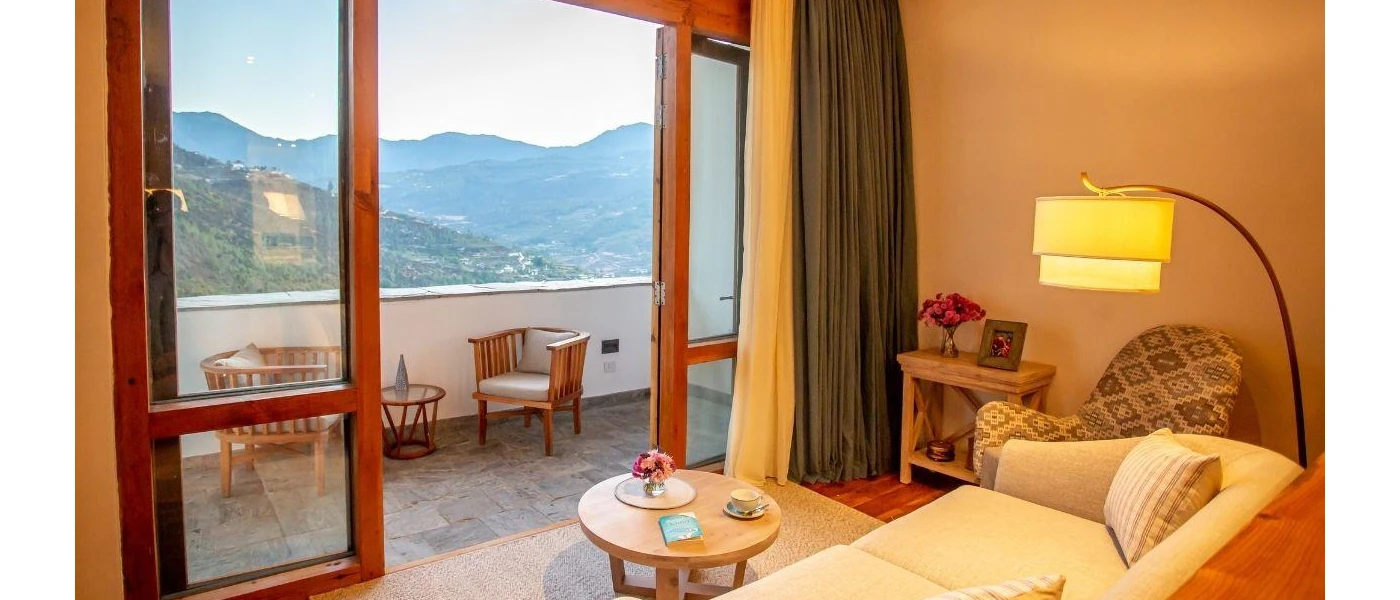 Ivory cushioned sofa with a looping floor lamp, overlooking a coffee table and furnished balcony with mountain views