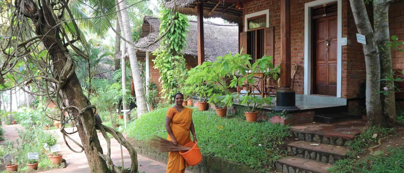 Smiling staff member in an orange sari fills a bucket in the tropical gardens