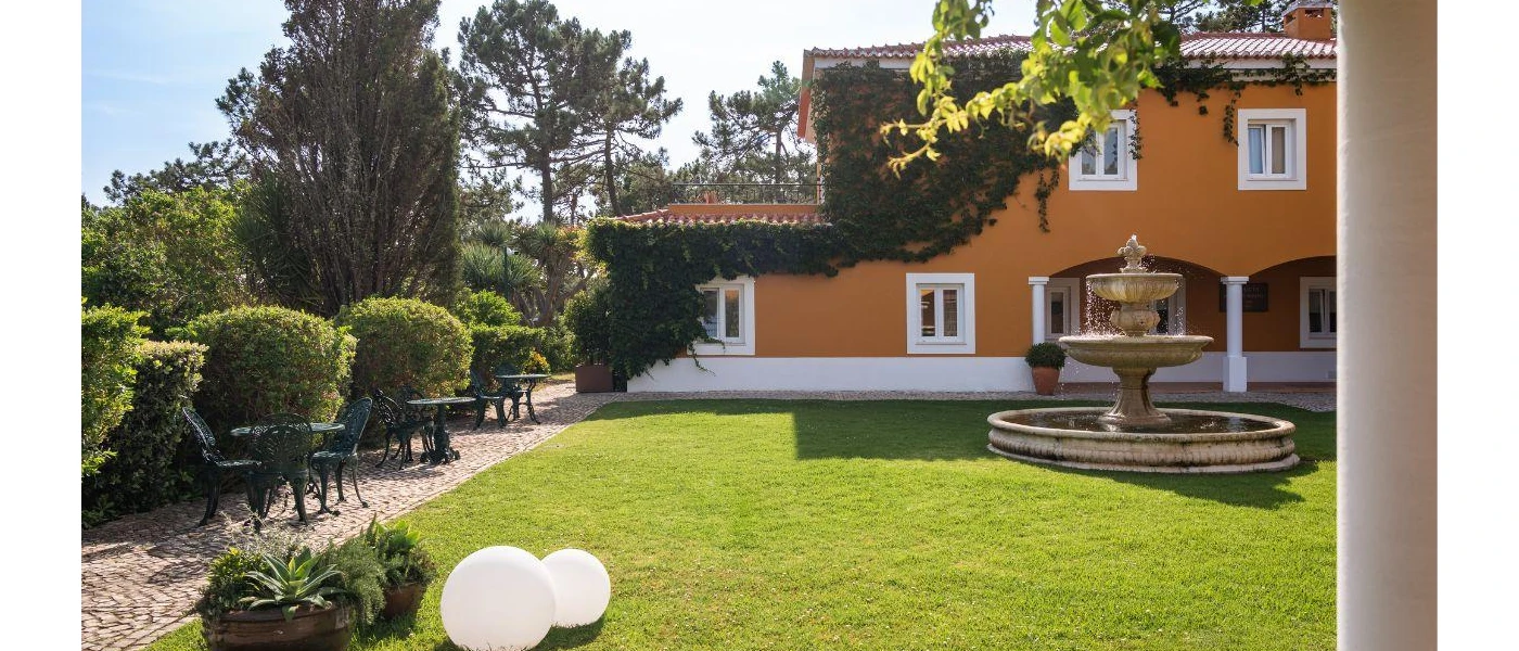 Mustard building with white window panes, in a lawned garden with a water fountain