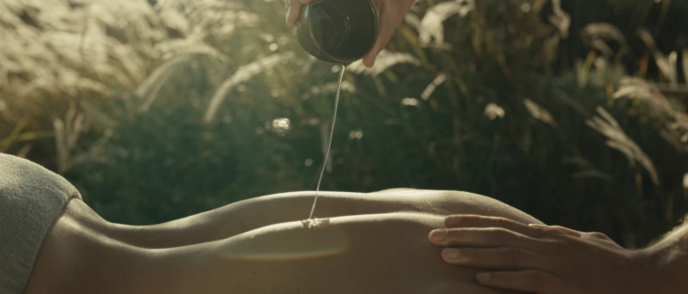 Therapist pours oil on a guest's back during an outdoor spa treatment